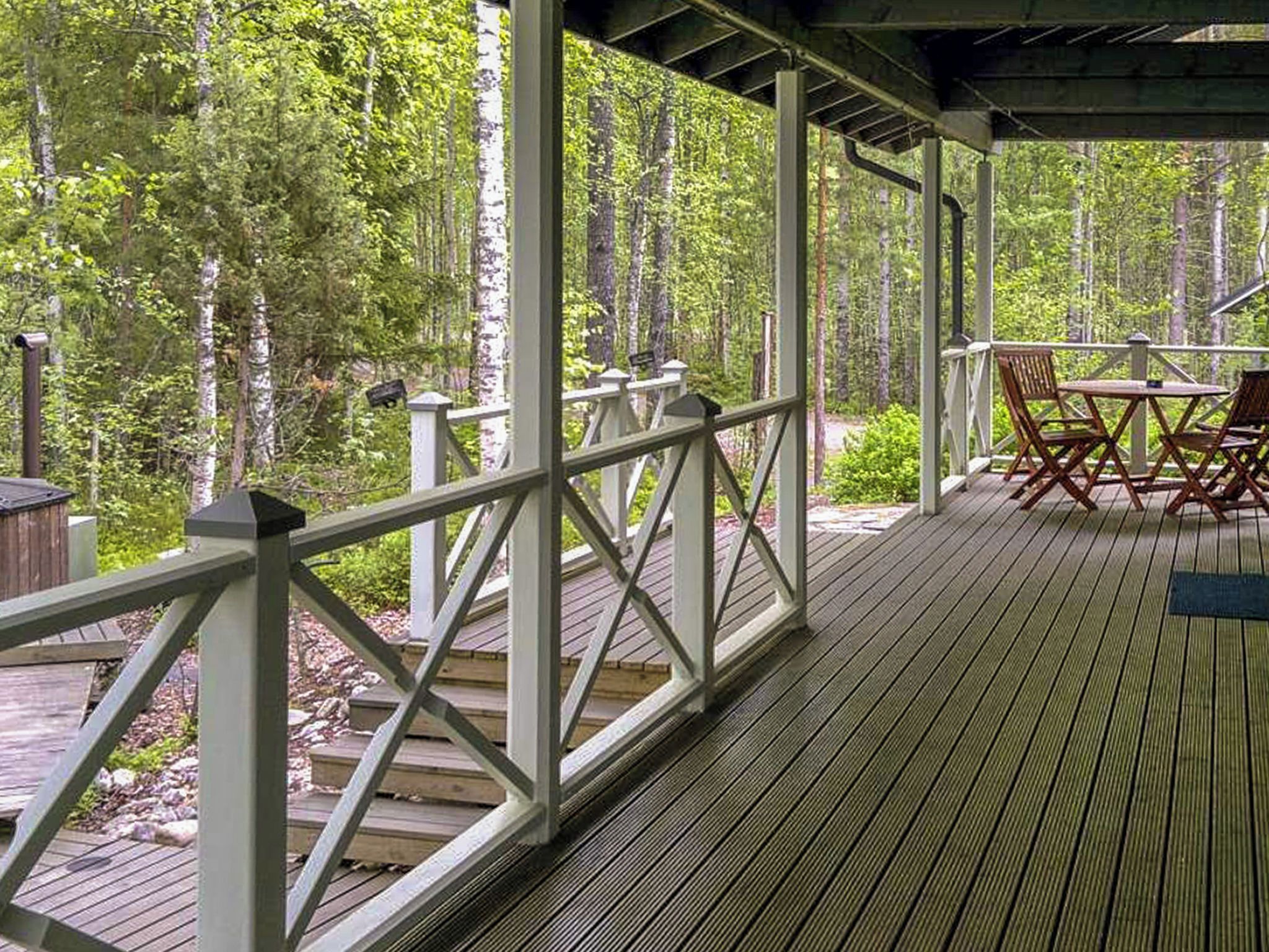Eine überdachte Terrasse mit Geländer, Holzboden und einem Tisch mit Stühlen.