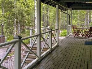 Een overdekt terras met een leuning, houten vloer en een tafel met stoelen.