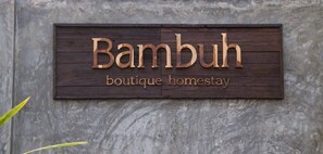 Ein Holzschild mit dem Aufdruck "Bambuh boutique homestay" an einer Betonwand befestigt.
