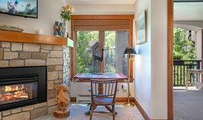 Relax in this inviting living room with a fireplace, comfortable seating, and a dining table. Enjoy the view of the lush garden from the large window.
