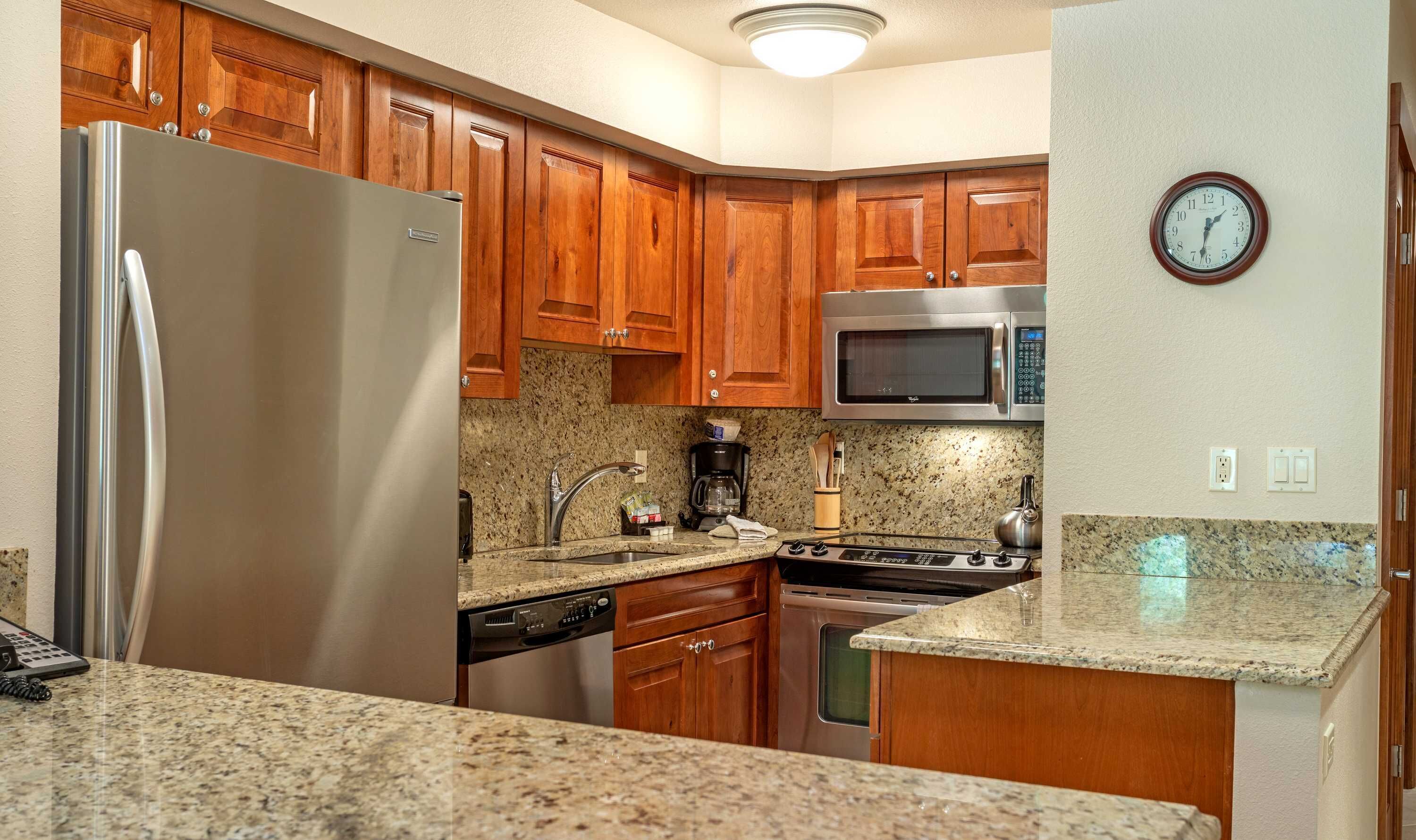 A kitchen with wooden cabinets, a stainless steel refrigerator, a microwave, a stove, and granite countertops.