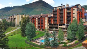 A multi-story hotel with balconies, a swimming pool, and a mountainous backdrop. - Ski In and Out Condo in Lionshead Village w/ Pool, Hot Tubs, and Lovely Views (Vail)