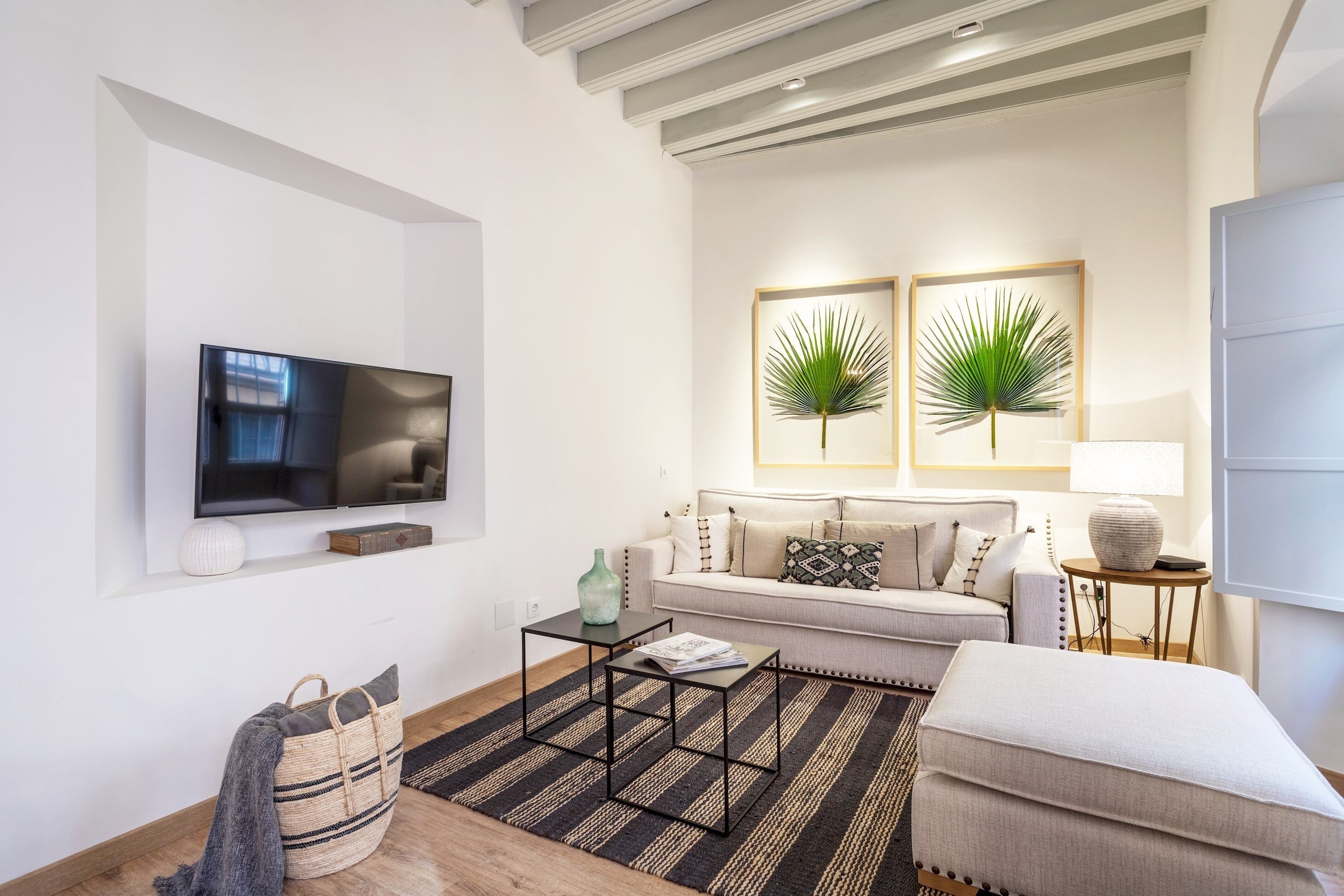 Ein modernes Wohnzimmer mit Flachbildfernseher, Sofa, Couchtisch und zwei Bilder mit Pflanzen.