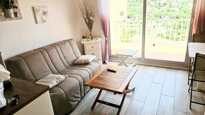 Una sala de estar acogedora con sofá, una mesa de centro de madera y un balcón con vistas a zonas verdes.