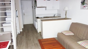 Un espacio habitable compacto con kitchenette, un sofá y una mesa de madera.