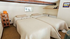 Un dormitorio pequeño y acogedor con dos camas individuales, una silla de madera, una estantería con libros y un espejo en la pared.