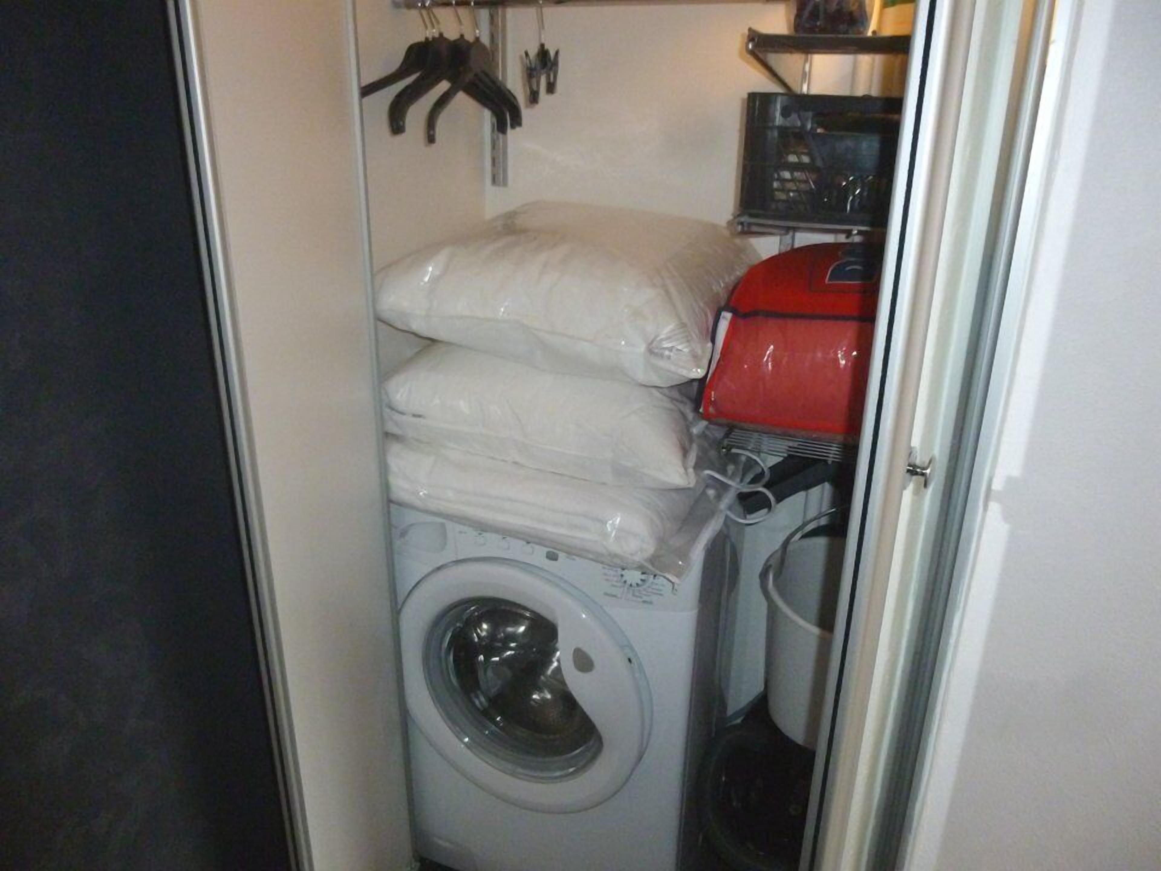 A compact laundry room with a front-loading washing machine, stacked white linens, and a red dryer.