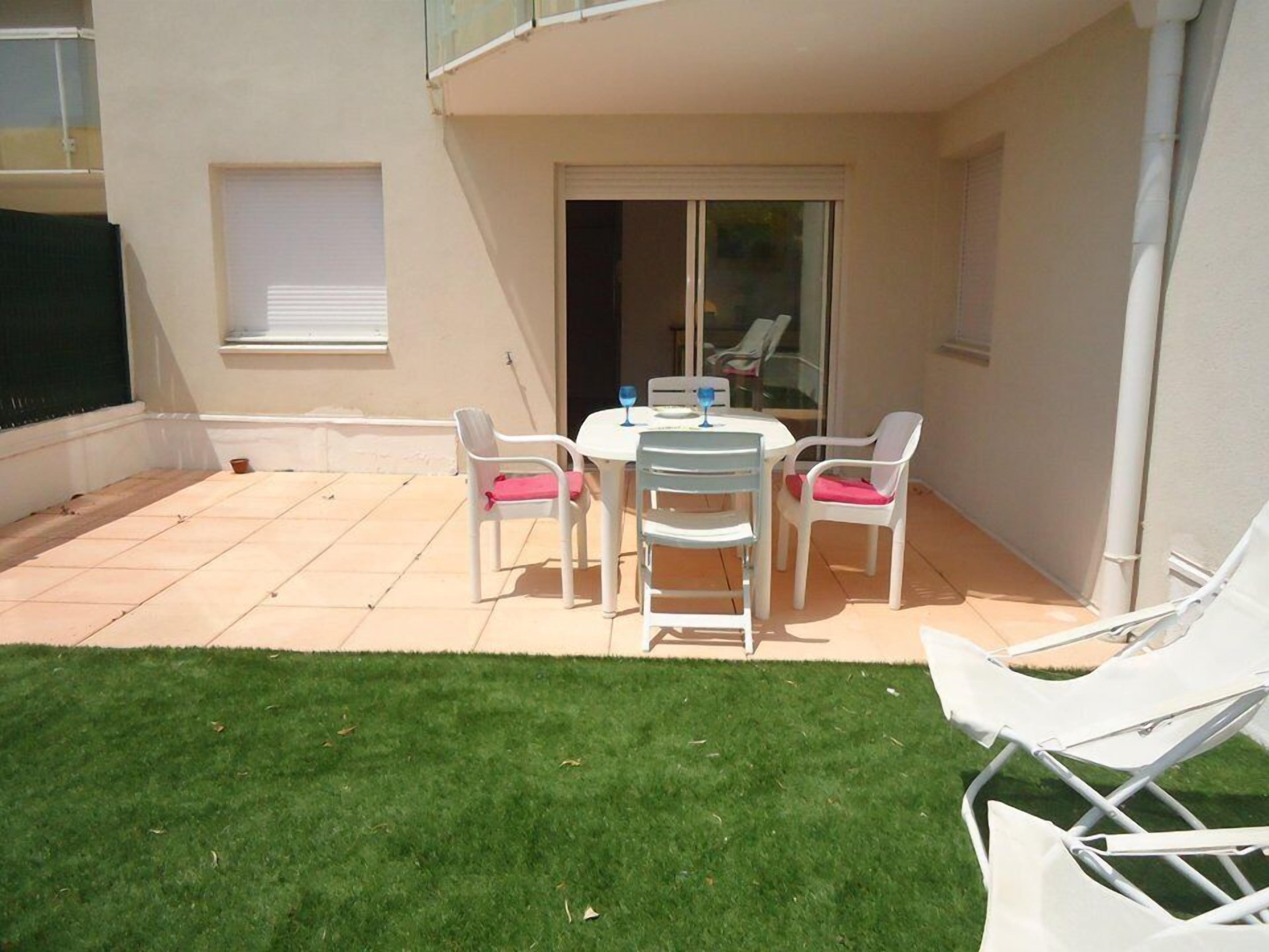 A patio with a table and chairs, a grassy area, and a building with a sliding door.
