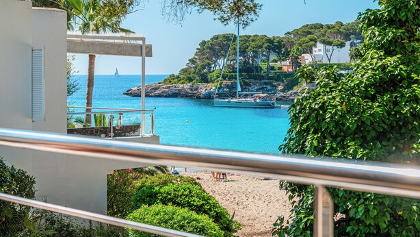 A coastal view with a beach, a sailboat, and a white building with a balcony. - B23. Beachfront apartment with pool, AC, wifi (Cala d'Or)