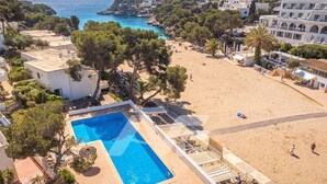 A pool adjacent to a beach with a view of the sea and surrounding buildings. - B23. Beachfront apartment with pool, AC, wifi (Cala d'Or)