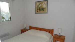 Een slaapkamer met een houten bed, twee nachtkastjes met lampen, een raam en een schilderij van orchideeën aan de muur.