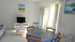 Een kamer met een eettafel, stoelen, een televisie op een dressoir en een schilderij aan de muur.