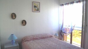 A bedroom with a bed, two bedside tables with lamps, a window with curtains, and two wall-mounted pictures. - 2-room air-conditioned apartment, swimming pool (CAVALAIRE sur mer)