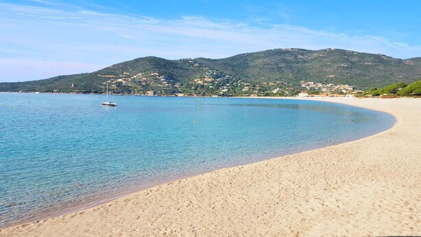 A beach with clear blue water, a sandy shore, and a sailboat in the distance. - Studio with separate bedroom. Terrace sea view. Bay of Sagone (Sagone)