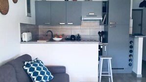 A modern kitchen with grey cabinets, a central island, and a dining area with a grey sofa and a coffee table. - Studio with separate bedroom. Terrace sea view. Bay of Sagone (Sagone)