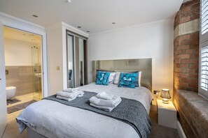 Ein modernes Schlafzimmer mit einem großen Bett, einer Glasdusche, einer Ziegelfassade und einer Nachttischlampe.
