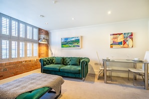 A room with a green sofa, a painting, a dining table with chairs, and a window with blinds. - Cocoa Suites 46 - One bedroom apartment in York city centre (sleeps 2) (York)