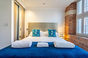Quarto de hotel com uma cama grande, uma parede de tijolos e uma janela com persianas.