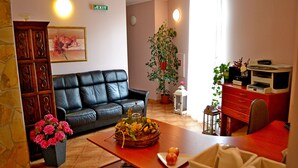 Una sala de estar con un sofá de cuero, una mesa de comedor con una cesta de frutas, una planta en maceta e una impresora sobre un escritorio.