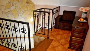 Una habitación con pared de piedra, un sillón de cuero marrón, una mesa de madera con un jarrón y una manzana, y una partición metálica negra.