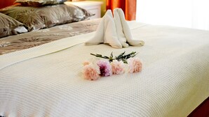 Una cama bien hecha con toallas blancas dobladas al pie, un arreglo floral decorativo y un cabecero de madera.