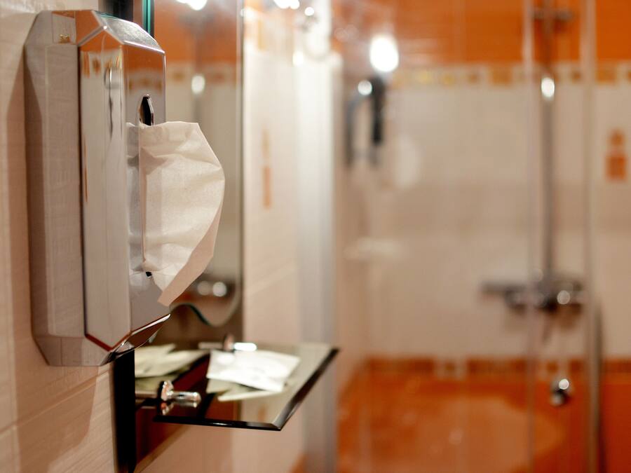 A restroom with a paper towel dispenser, a mirror, and a glass shower enclosure.