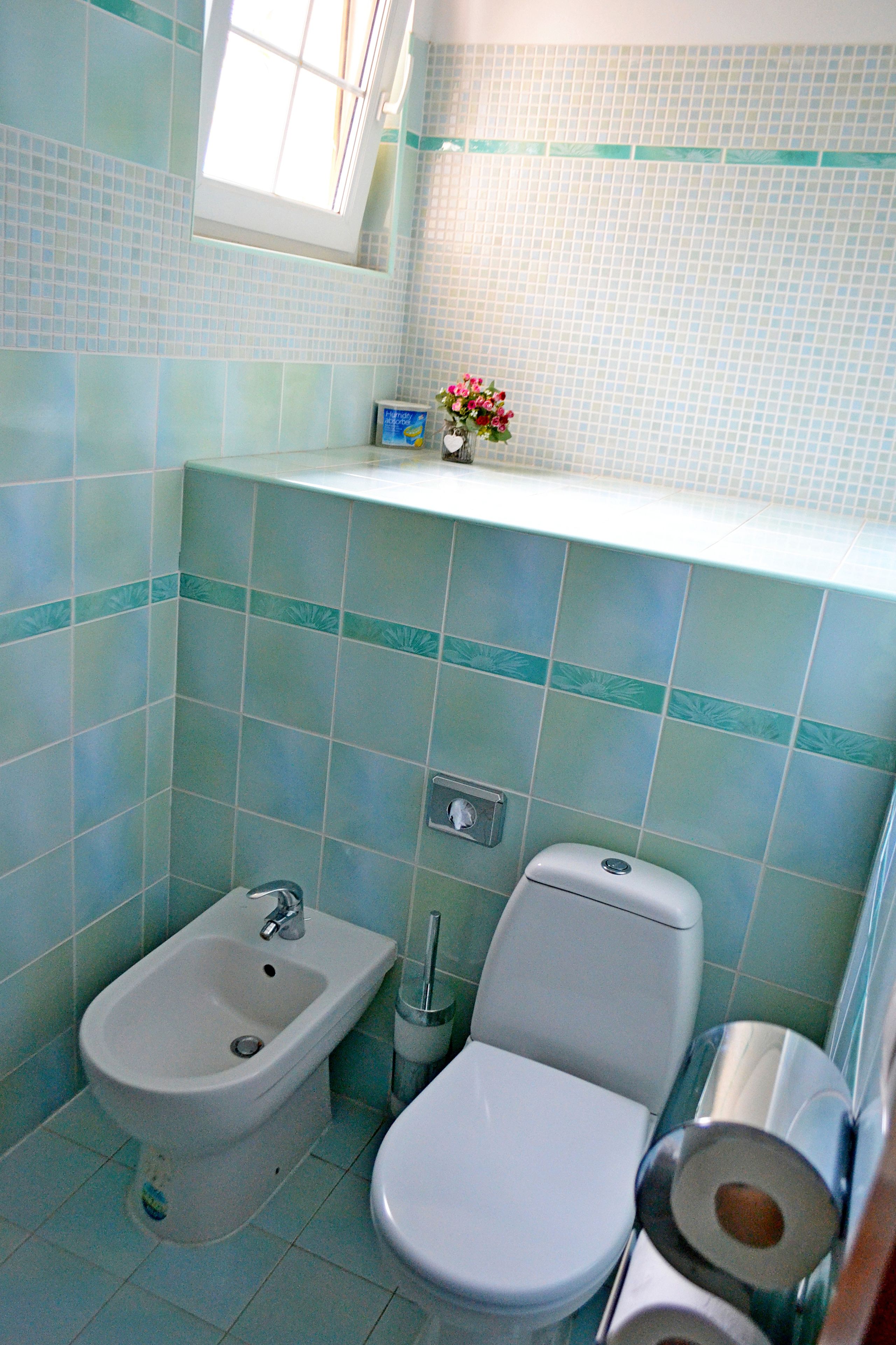 A bathroom with a bidet, toilet, and a shelf with a vase of flowers.