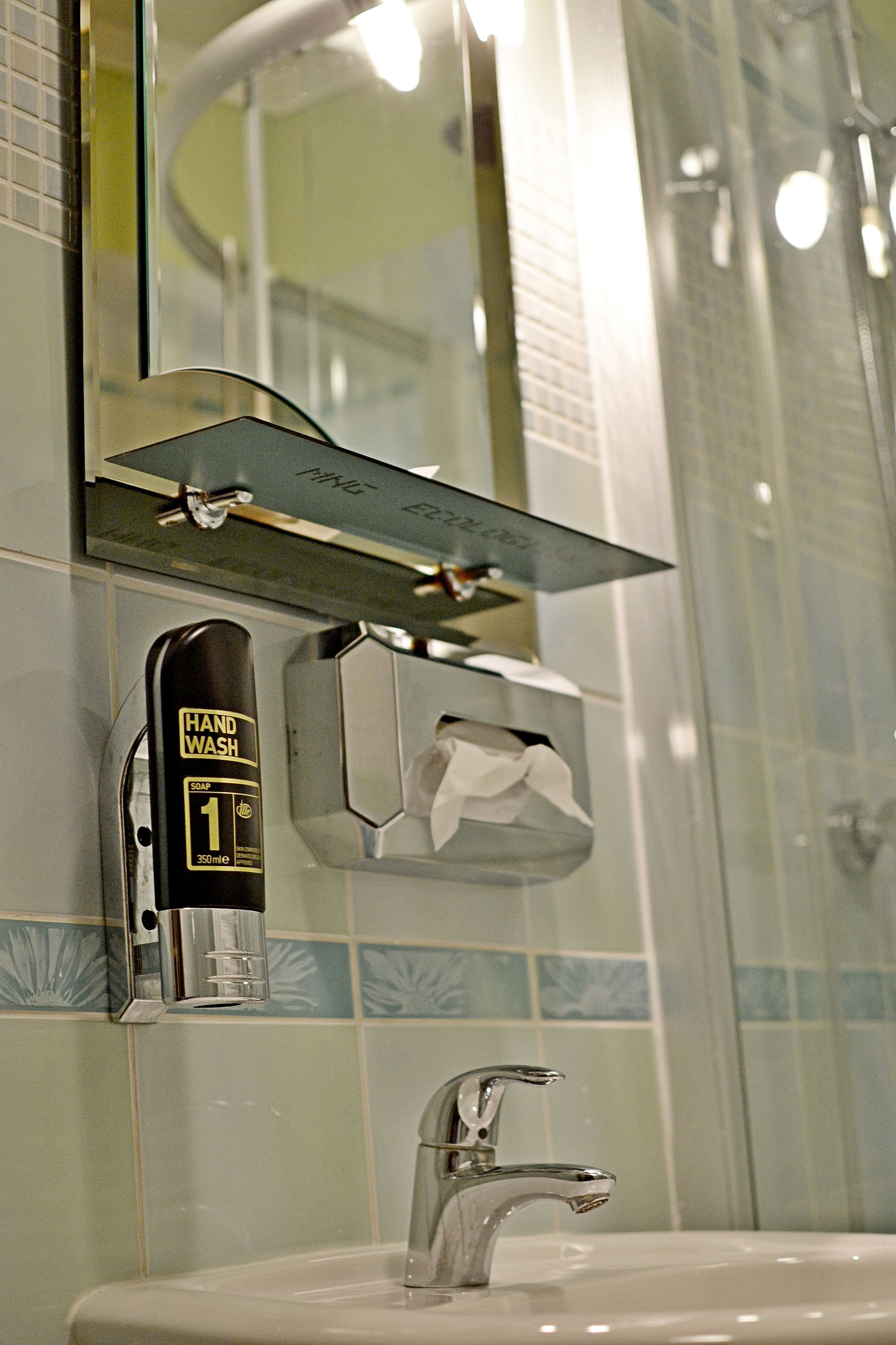 Een badkamer met een zeepdispenser, een pak tissues en een wastafel.