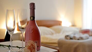 A bottle of champagne and two glasses on a table with a bed in the background.