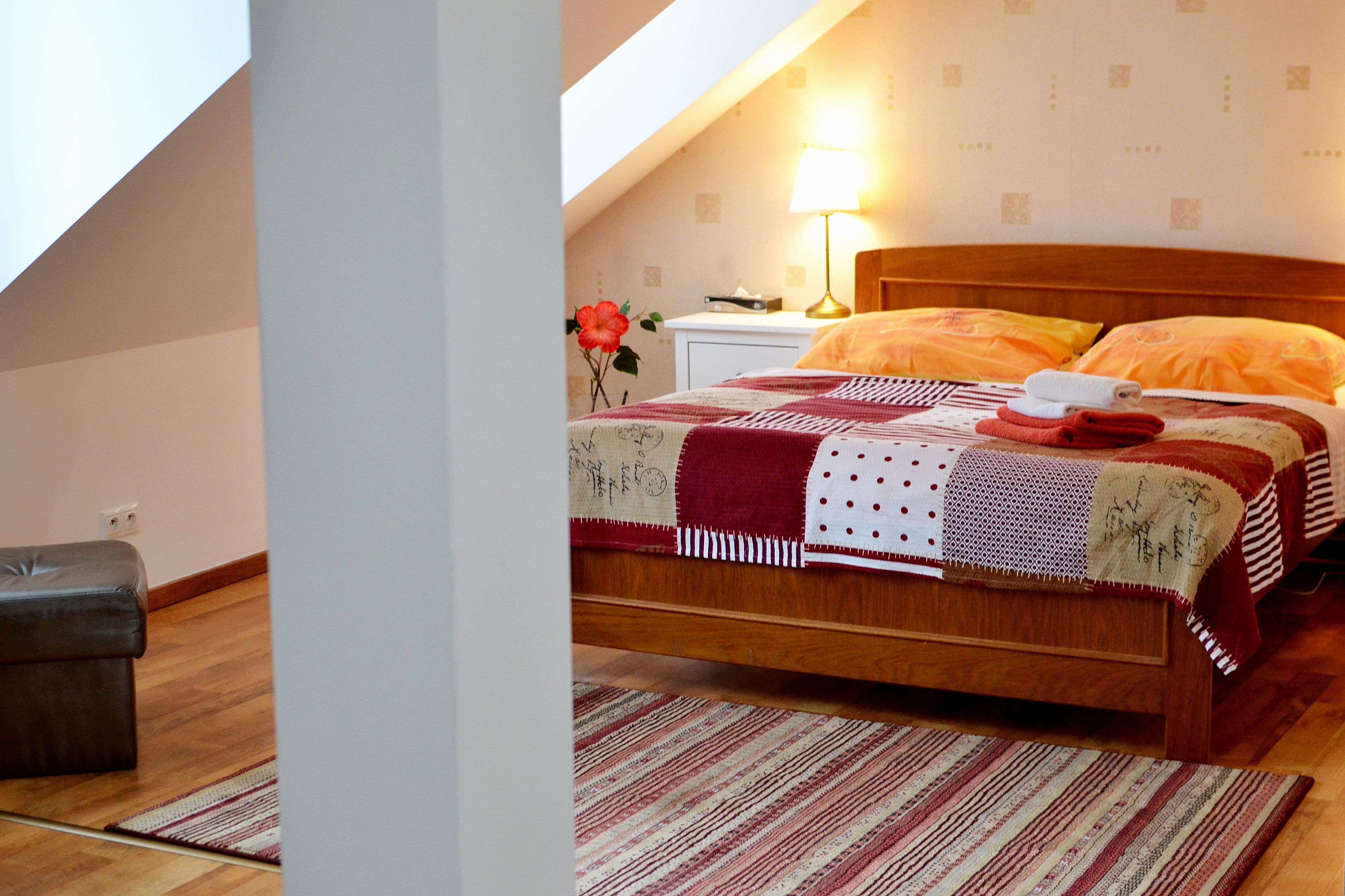 Une chambre à coucher avec un lit en bois, une table de chevet, une lampe et une fleur rouge posée sur la table de chevet.