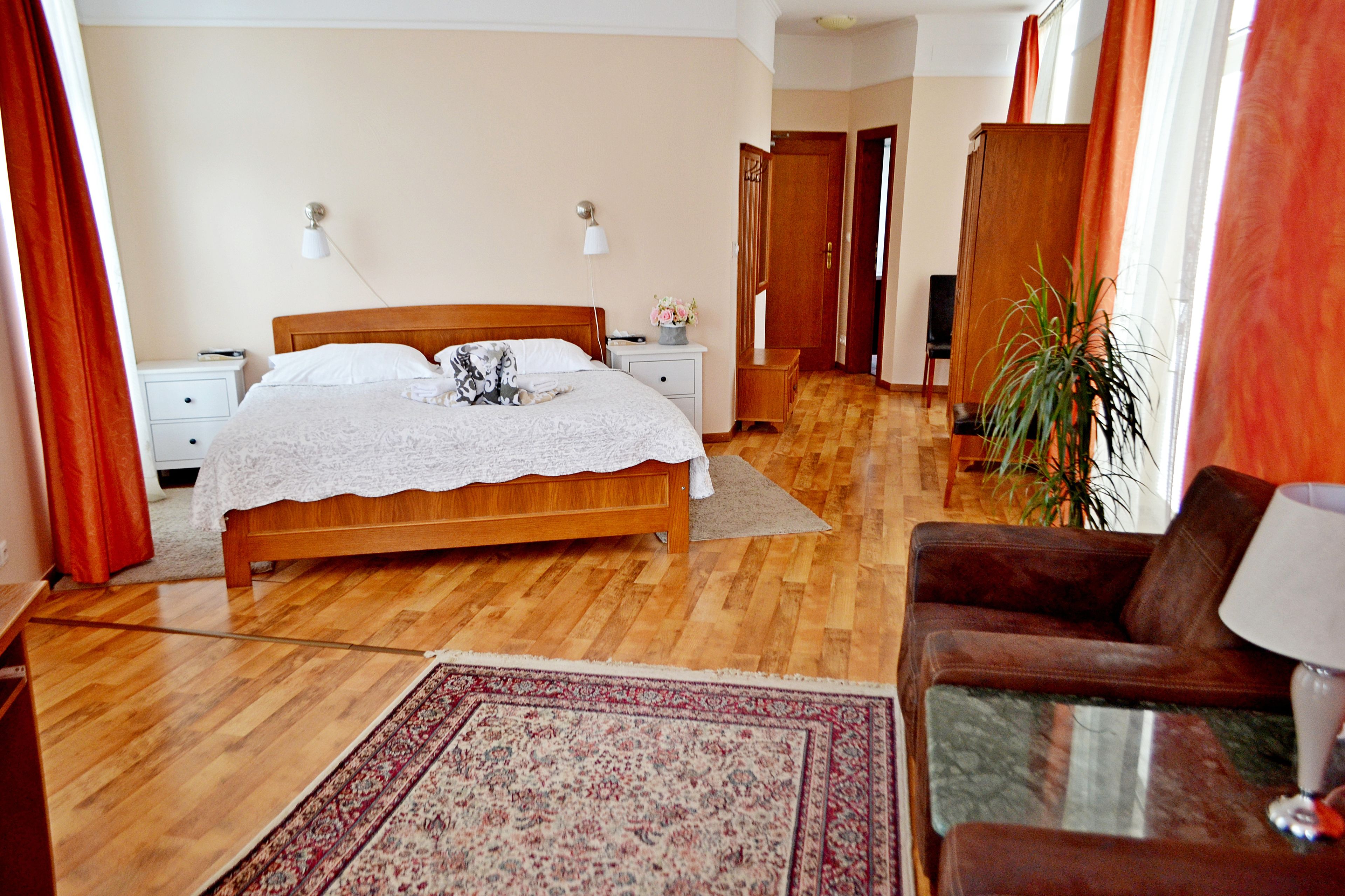 A bedroom with a wooden bed, nightstands, a desk, a chair, and a large plant.