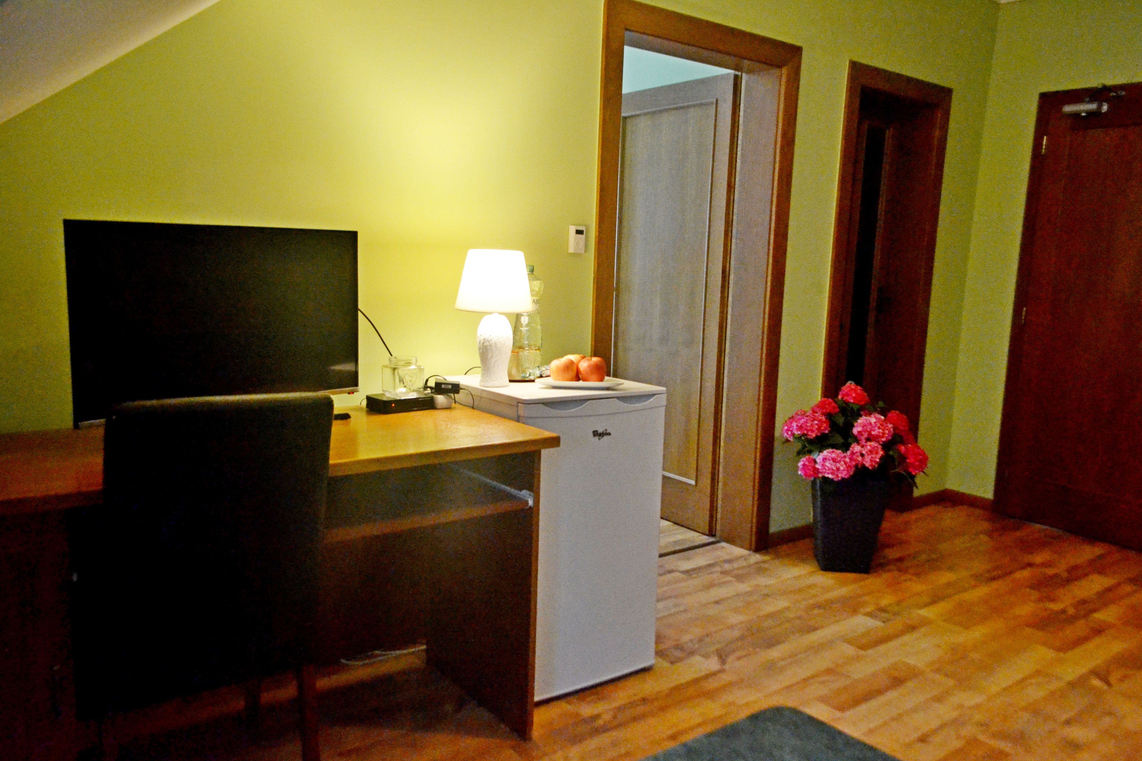 A compact room with a wooden desk, a chair, a small white appliance, a lamp, and a potted plant.