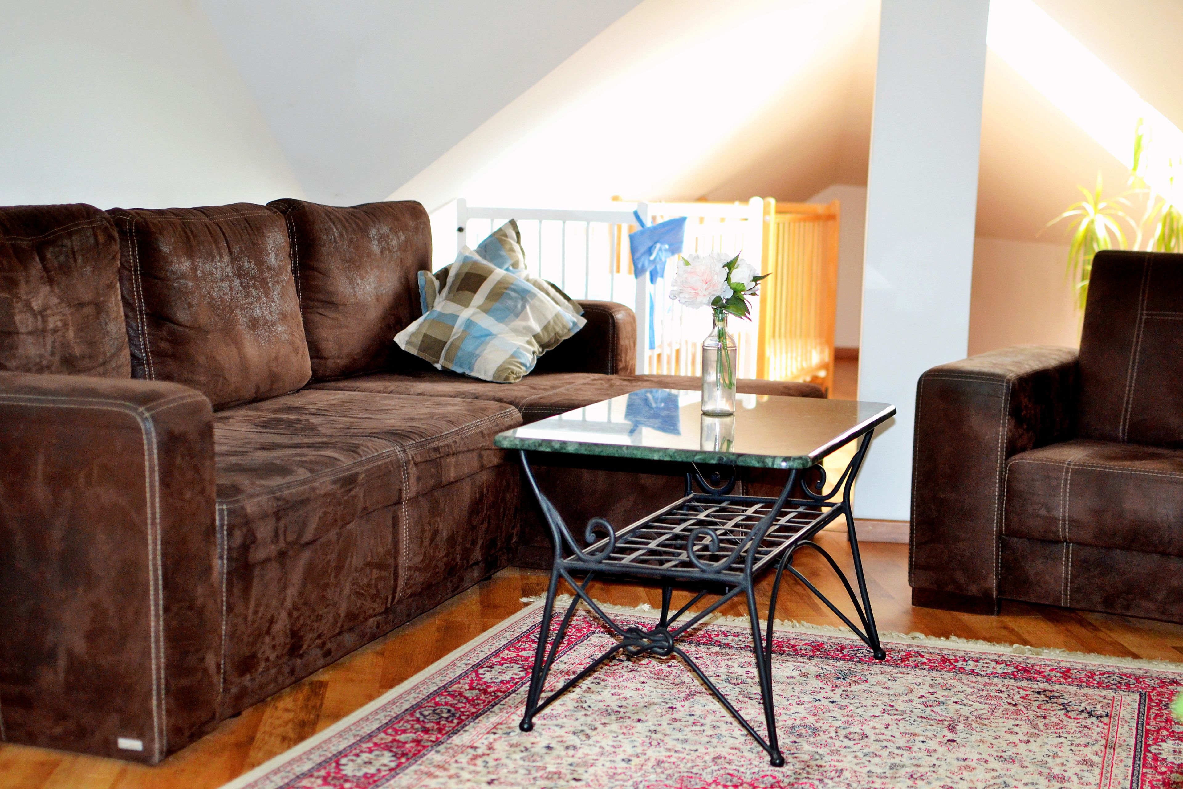 A cozy living room with a brown leather sofa, a glass-top coffee table, and a patterned rug.