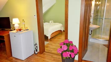 A bedroom with a bed, a nightstand with a lamp, a refrigerator, and a flower vase.