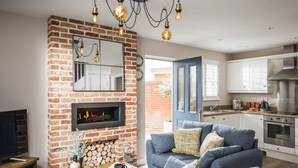 A modern living room with a brick fireplace, a sofa set, and a kitchen area with stainless steel appliances.