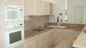 A kitchen with light wooden cabinets, a white oven, a granite countertop, and a sink. - Contemporary apartment with air conditioning in a residence with swimming-pool (CAVALAIRE sur mer)