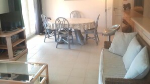 A living room with a sofa, a dining table with chairs, a TV, and a painting on the wall. - Contemporary apartment with air conditioning in a residence with swimming-pool (CAVALAIRE sur mer)