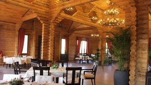 Un restaurant aménagé dans un style de chalet en rondins, avec des murs et des plafonds en bois, des lustres et des tables dressées pour le service.