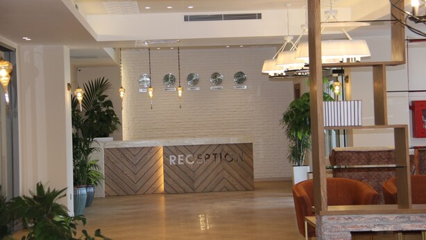 Un espace d’accueil doté d’un comptoir de réception à motifs en chevrons, de plusieurs horloges et de luminaires suspendus.