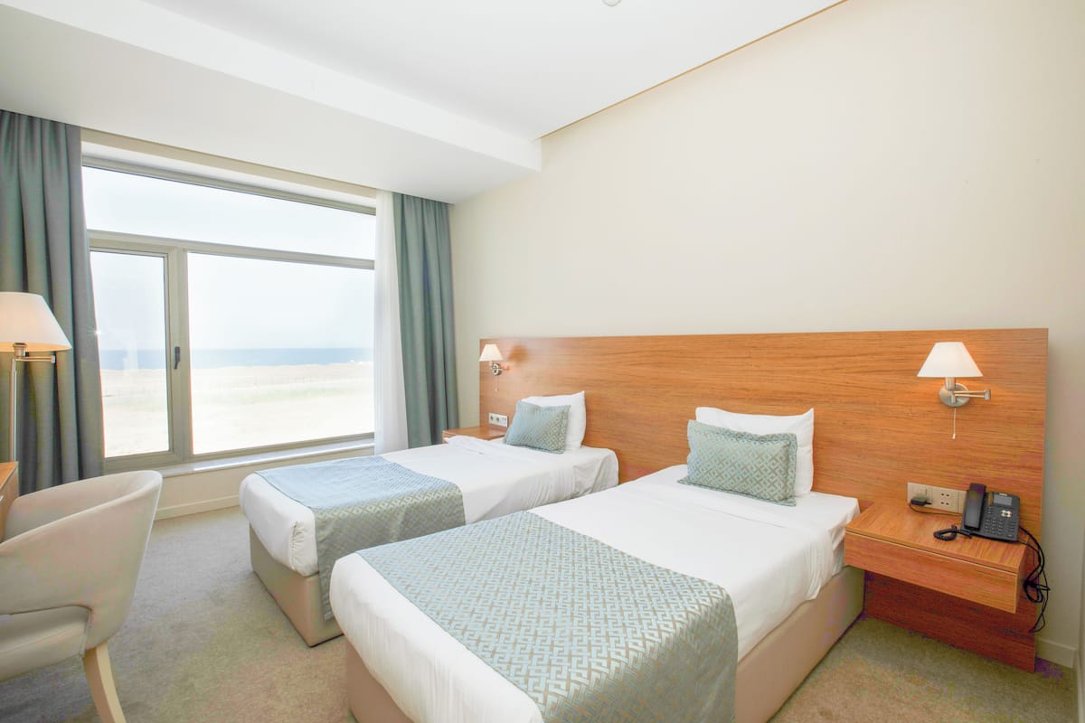 Une chambre d’hôtel avec deux lits, un bureau, une chaise et une grande fenêtre donnant sur un paysage agréable.