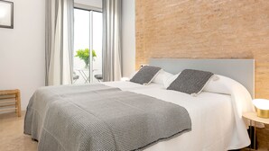 A modern bedroom with a large bed, striped curtains, a brick wall, and a small table with a lamp. - Genteel Home Santa Teresa III (Sevilla)
