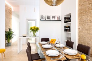 Un espace repas moderne avec une table en verre, des chaises foncées et un mur blanc orné de tableaux.