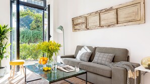 A living room with a glass coffee table, a grey sofa, and a view of greenery outside. - Genteel Home Santa Teresa III (Sevilla)