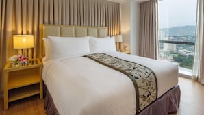 Une chambre d’hôtel avec un grand lit, deux tables de chevet avec des lampes, une vue sur la ville par une grande fenêtre et un mur recouvert de rideaux.