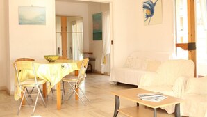 Ein helles Wohnzimmer mit einem weißen Sofa, einem Esstisch mit Stühlen und einem Couchtisch aus Holz.