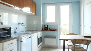 Eine kleine Küche mit weißen Schränken, einem Toaster, einer Kaffeemaschine und einem Essbereich mit Tisch und Stühlen.