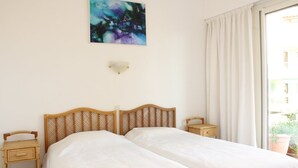 Ein Zimmer mit zwei Betten, einer Wandleuchte und einem Fenster mit Vorhängen.