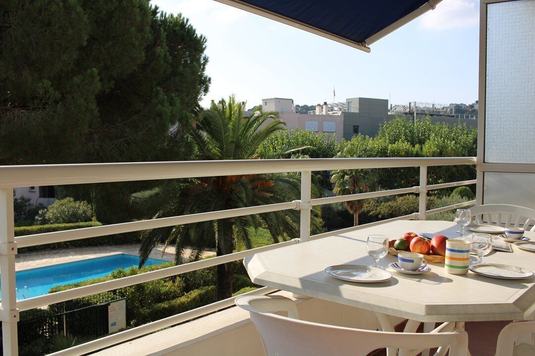 A balcony with a pool view, white furniture, and a table set for dining.