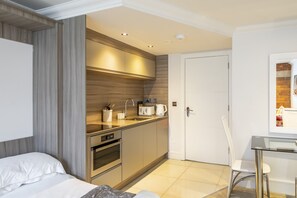 A modern hotel room with a kitchenette, a bed, a glass table, and a white chair. - Cocoa Suites 49 - York city centre studio (sleeps 2) (York)