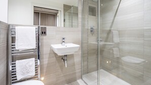 A modern bathroom with a glass shower enclosure, a sink, and a towel rack with neatly folded towels. - Cocoa Suites 49 - York city centre studio (sleeps 2) (York)